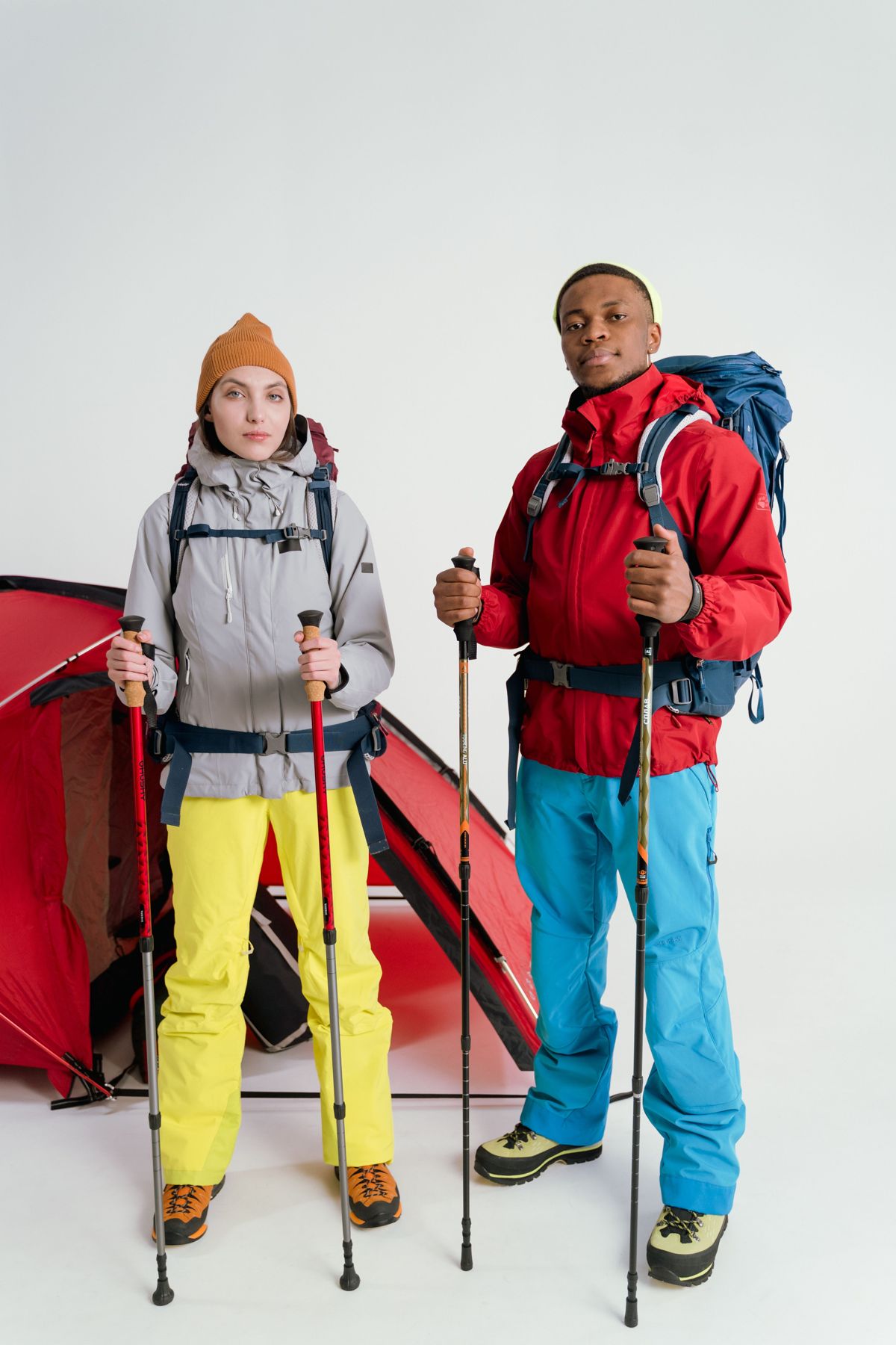 Two hikers with backpacks and trekking poles standing in front of a red tent