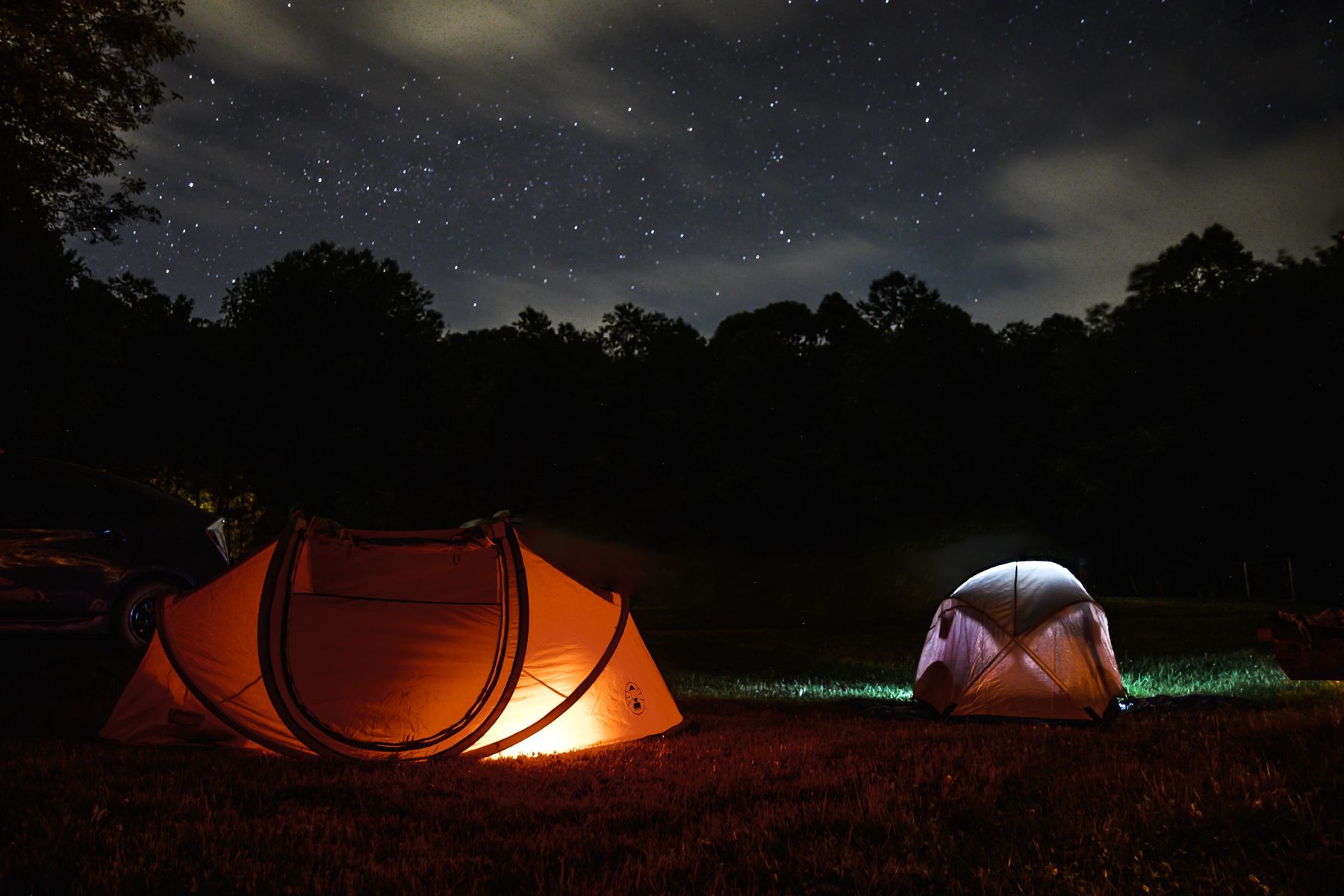 Glowing orange pop-up tent and white dome tent under a starry night sky