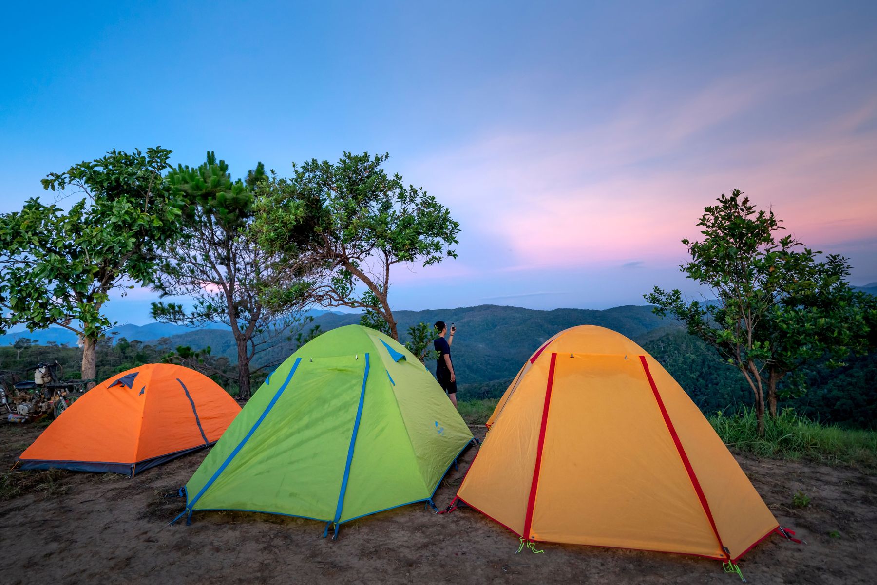 Orange, green and yellow dome tents pitched on a hilltop at sunset